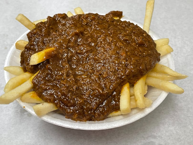 A white bowl filled with golden french fries generously topped with a thick, rich brown chili.