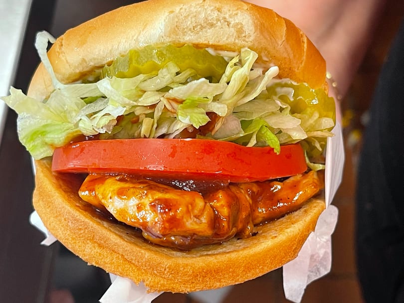 Close-up of a BBQ chicken sandwich with lettuce, tomato, and pickles on a bun.