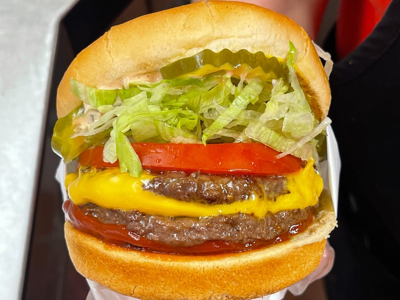 Close-up of a double cheeseburger with lettuce, tomato, pickles, and special sauce on a bun.